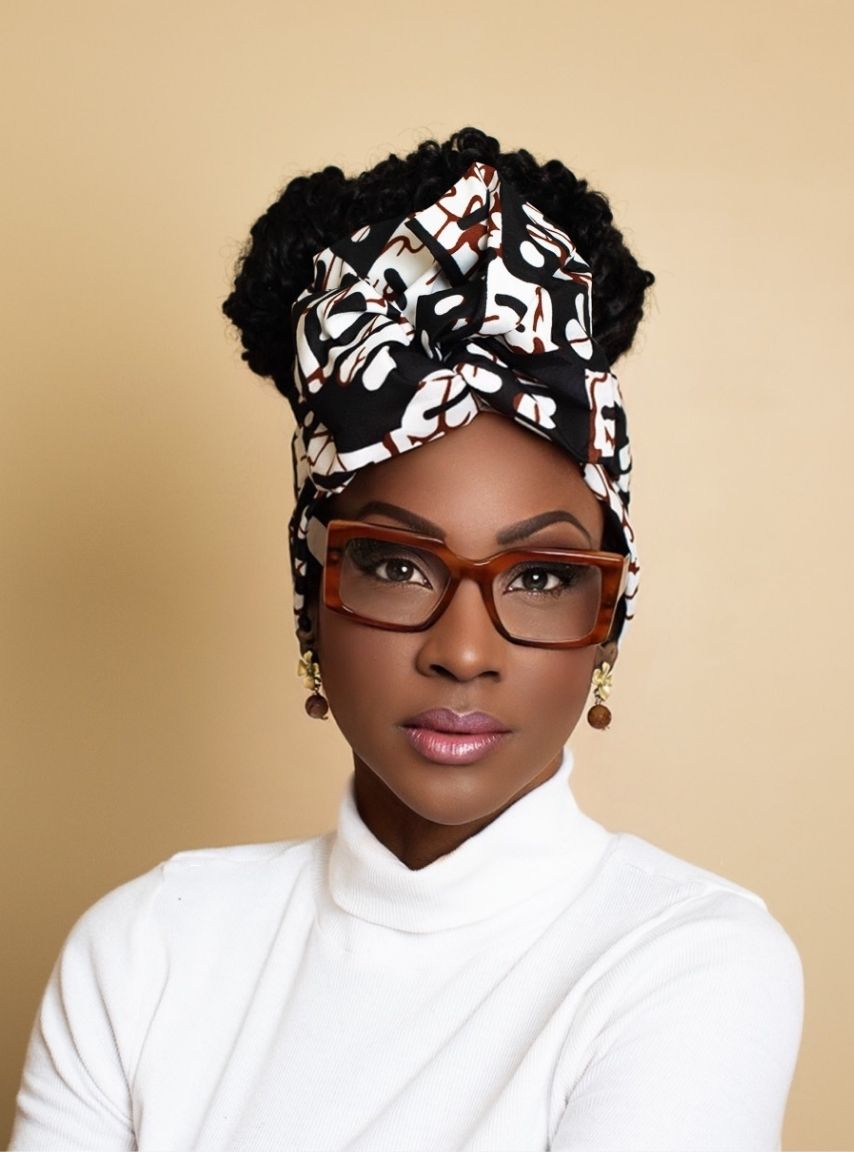 Woman wearing a patterned headscarf and glasses against a beige background